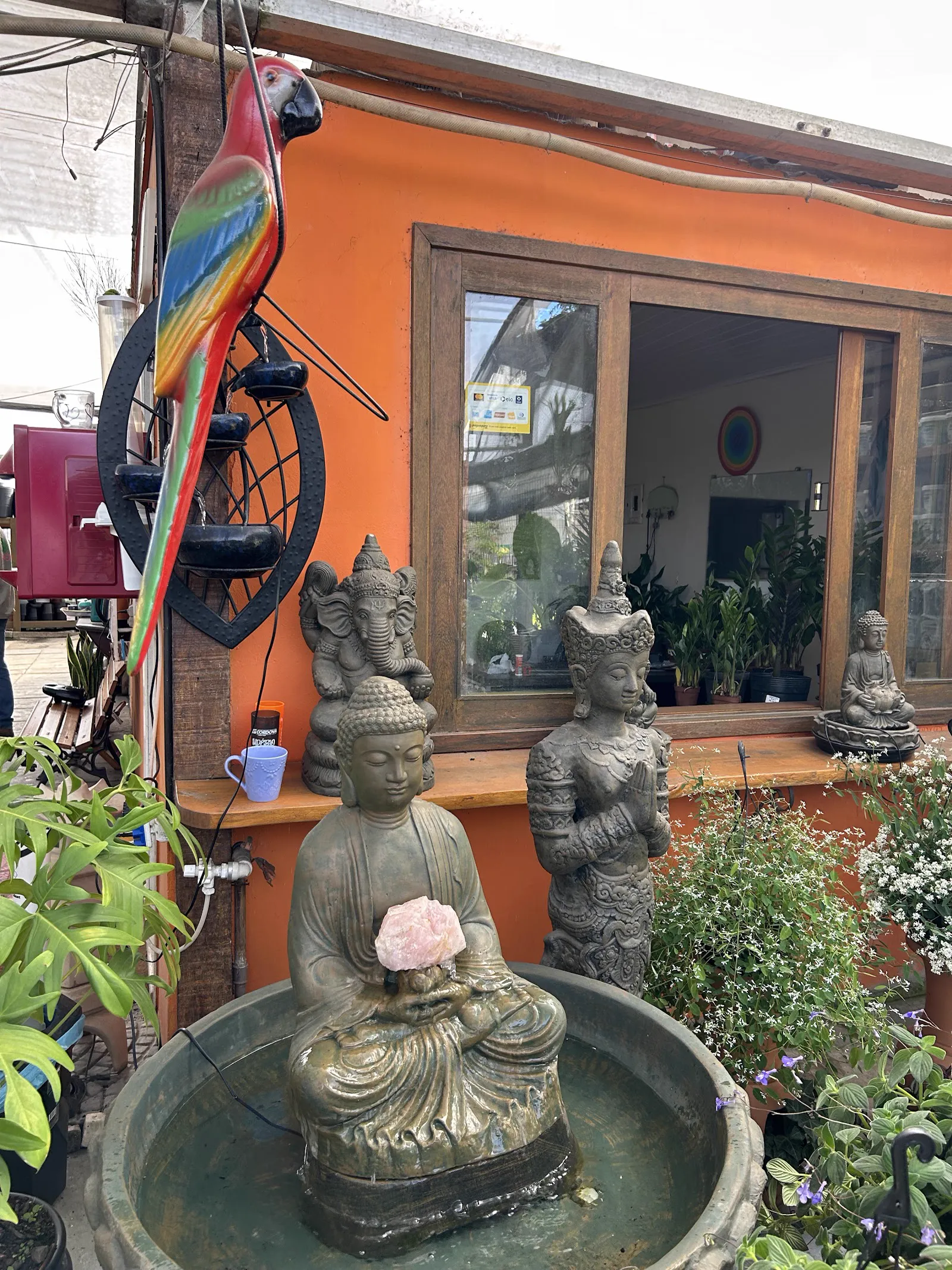 Fachada laranja da loja, com a arara decorativa, estátuas e a fonte