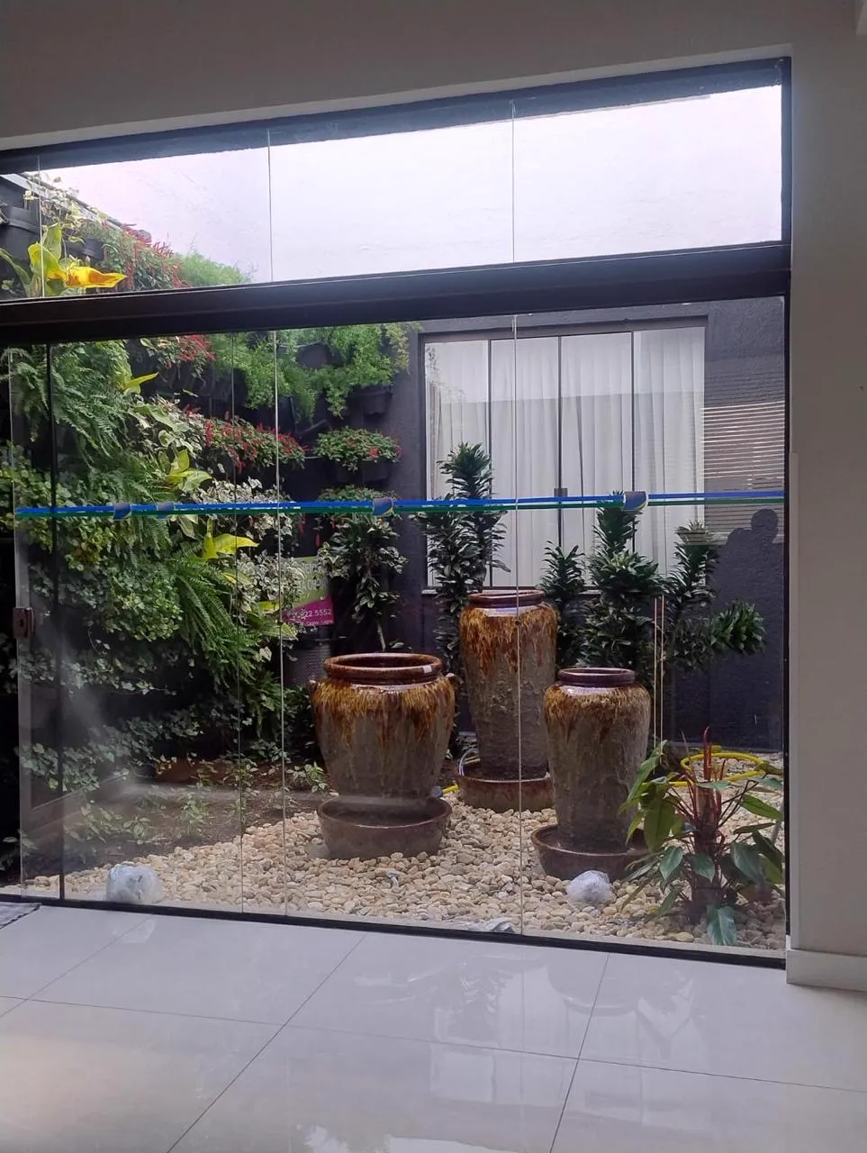 Jardim de inverno com jardim vertical, vasos grandes e pedras brancas